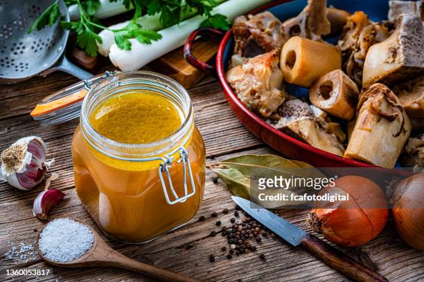 bone broth and ingredients on rustic table - bouillon stock pictures, royalty-free photos & images