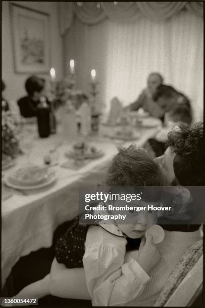 View of an unidentified two and half year old as she rests on her mother's shoulder during a Shabbat dinner, Oakland, California, March 15, 1996.