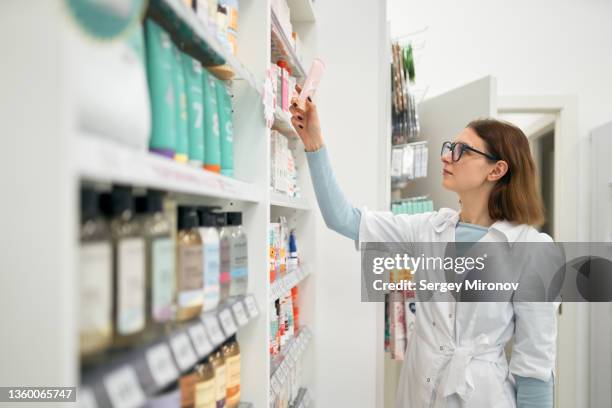 pharmacist taking medical cream from shelf - pharmaceutical industry stock pictures, royalty-free photos & images