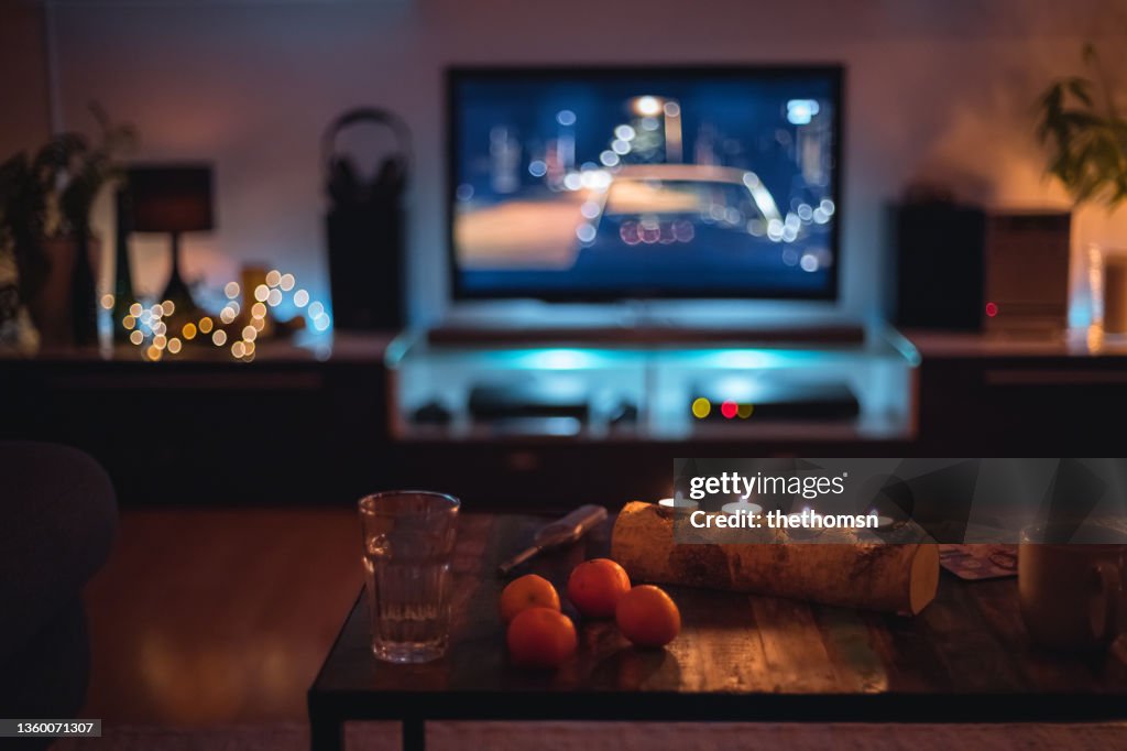 Dark indoor scene with candles, clementines and fairy lights in front of a TV, Germany