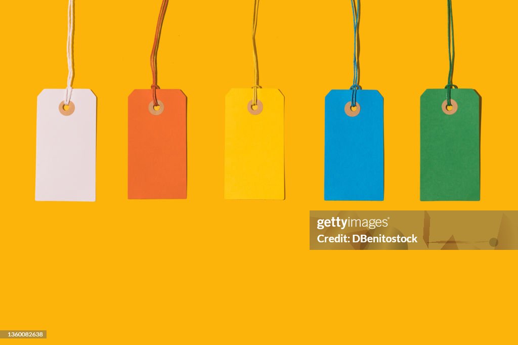 Five white, orange, yellow, blue and green cardboard price tags with string on yellow background. Pricing, ideas, groups, ordering, design and sales concept.