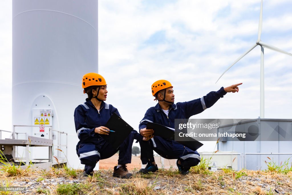 Young maintenance engineer team working in wind turbine farm , Technician and Engineer wearing safety harness PPE working at Wind Turbine farm