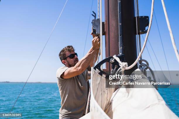 man tying ropes to the mast of a sailboat on the sea in a sunny day - shade sail stock pictures, royalty-free photos & images