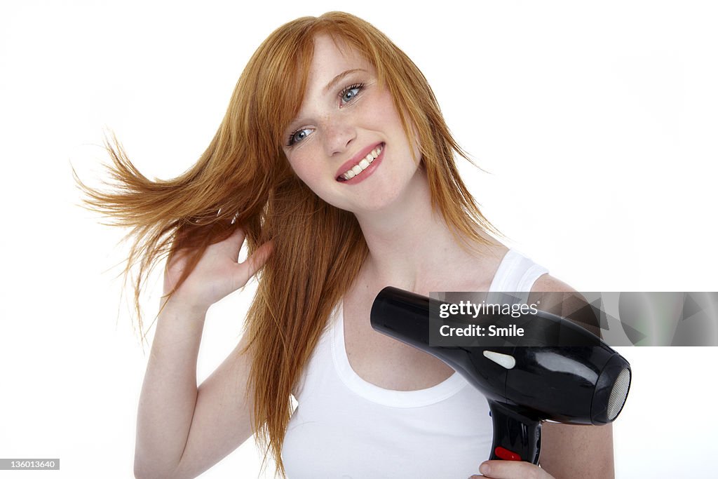 Young redhead blow drying her hair