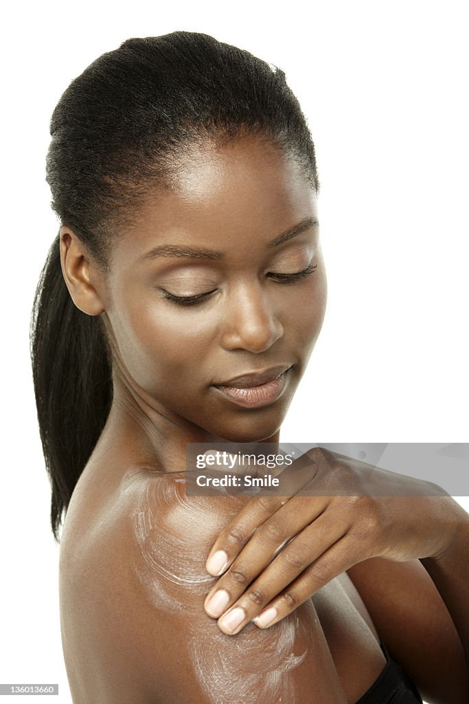 Young woman applying cream to her shoulder