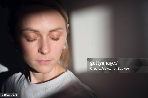 a lonely young sad calm girl or woman stands against a white wall, in a psychiatric clinic or at home, in the rays of sunlight, with her eyes closed. the concept of depression from illness and quarantine, fatigue and impotence. a copy of the space. - women in prison stock pictures, royalty-free photos & images