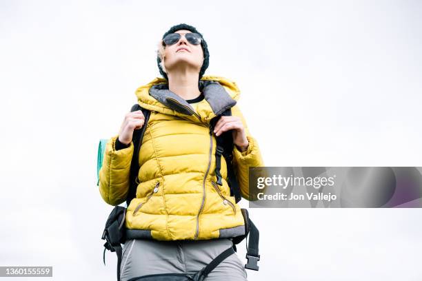 front view of a backpacker woman wearing sunglasses in warm clothing looking up against an illuminated background - daylight saving time 2021 stock pictures, royalty-free photos & images