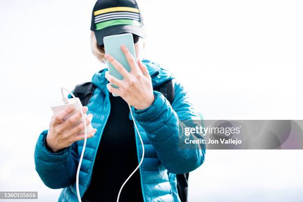 a traveler woman using her cell phone connected to a power bank - powerbank fotografías e imágenes de stock