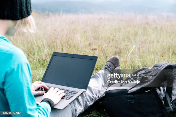 traveler woman using her laptop sitting on grass on a hillside. - looking behind stock pictures, royalty-free photos & images