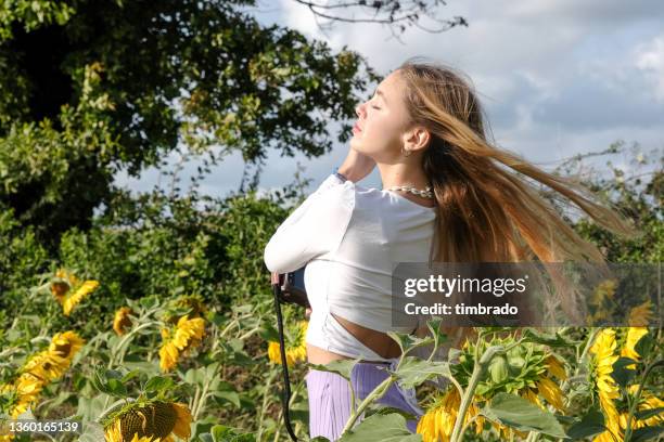 beautiful teenage girl standing in a sunflower field playing with her hair, france - 16 17 girl blond hair stock pictures, royalty-free photos & images