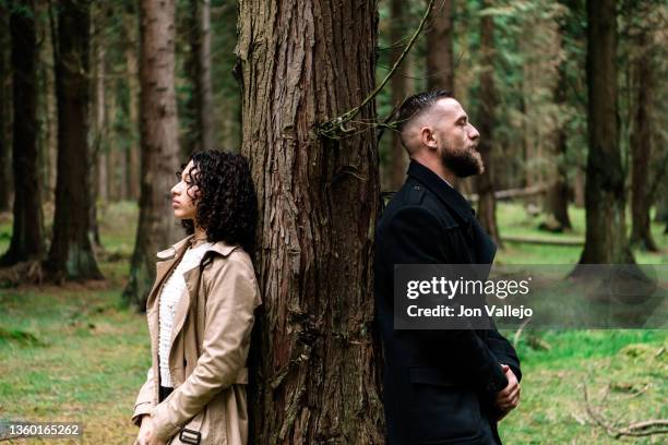 a woman and a man standing leaning each side against a tree in the forest. - menselijke relaties stockfoto's en -beelden