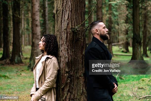 a woman and a man standing leaning each side against a tree in the forest. - relationship difficulties photos stock pictures, royalty-free photos & images