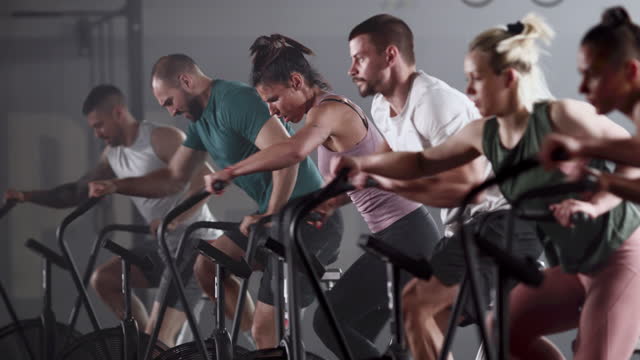 Group of determined athletes exercising on stationary bikes in a gym.