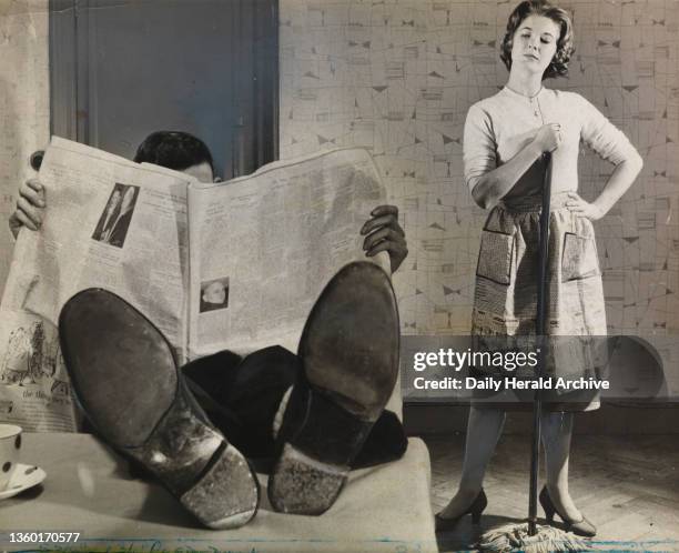 Man relaxes at home whilst his annoyed wife cleans the house. 15th May 1957.