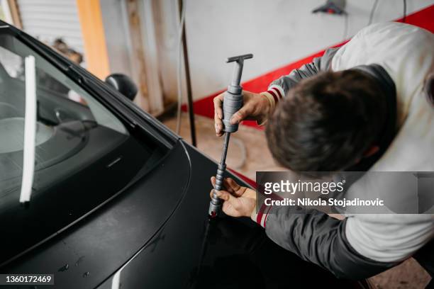 el técnico que usa guantes protectores está en proceso de reparación de abolladuras sin pintura en el automóvil - abollado fotografías e imágenes de stock