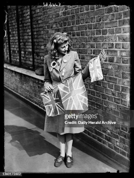 Woman holding Union flags, 1945. A photograph of a woman wearing badges and holding a number of flags, taken by Nixon for the Daily Herald newspaper...