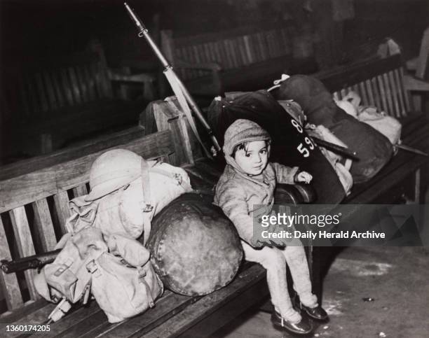 Small child sitting on a bench with soldiers' equipment, 28 December 1939. 'A small guardian of soldiers' equipment at Waterloo Station, London,...