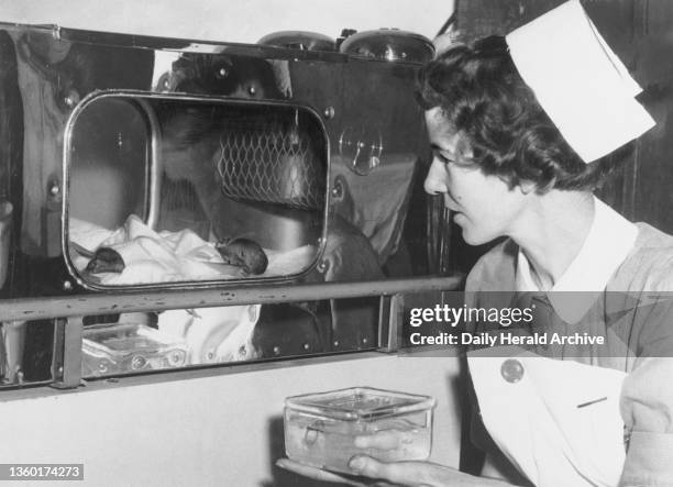 Baby lying in an incubator, circa 1955. A tiny baby lies in a hospital incubator, and is watched over by a nurse. "