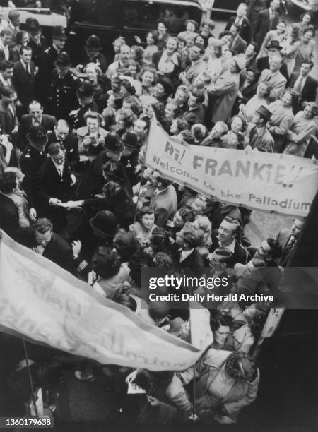 Frank Sinatra arriving at the London Palladium to make his debut in the UK, flanked on both sides by a police escort, he is mobbed by fans, some even...