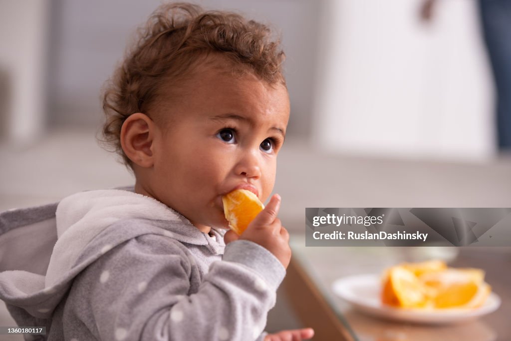 Baby eating orange fruit.