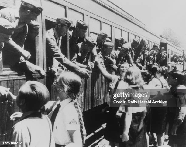 German troops on their way home from Spain, shown here in Vigo on a train surrounded by Hitler Youths and Hitler Maidens of the German colony, their...