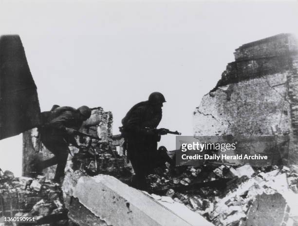 They fight on in the streets of Stalingrad'. Two men of the Red Army bending low and clambering over ruins, which once formed part of a normal city,...