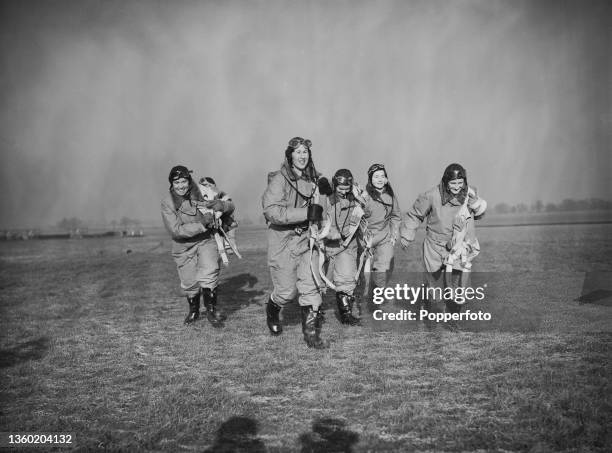 Five female ferry pilots from the Air Transport Auxiliary , wearing full flying suits, run towards their aircraft prior to flying from their base at...
