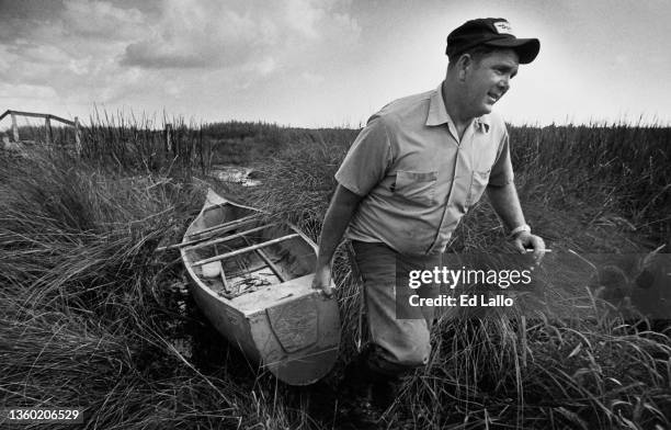 View of American alligator fisherman Steven Bourriaque , a cigarette in one hand, as he drags a pirogue through a swamp, Louisiana, October 7, 1980.