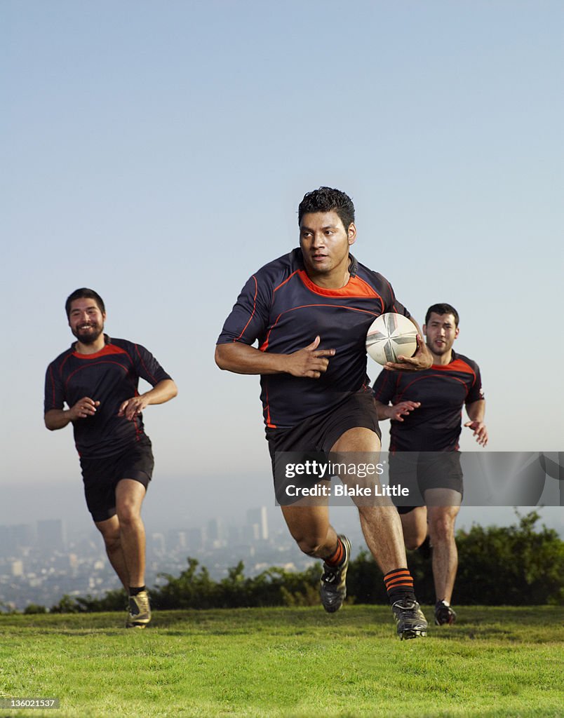 Three rugby players running on a field.