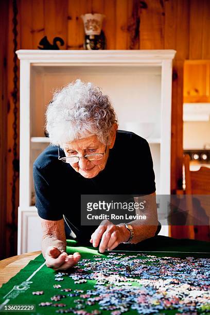 senior woman works on a jigsaw puzzle - senior puzzle stock pictures, royalty-free photos & images