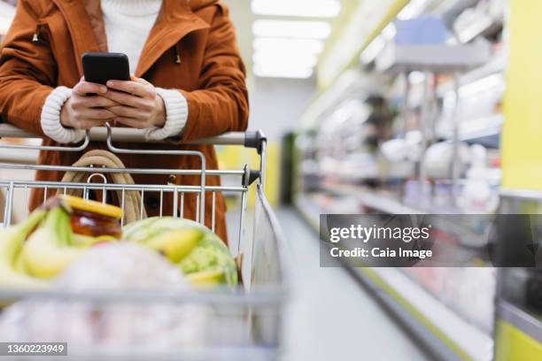 woman with smart phone pushing shopping cart in supermarket - caiaimage stock-fotos und bilder