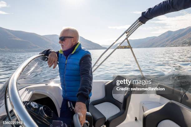 mature man pilots boat on calm lake waters - boat steering wheel stock pictures, royalty-free photos & images