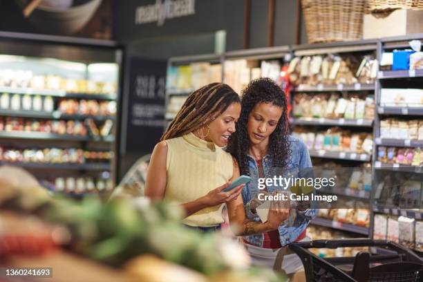 women with smart phone grocery shopping in supermarket - couple in supermarket stock-fotos und bilder