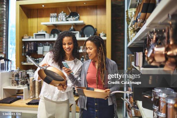 smiling women with smart phone shopping for frying pans - kitchenware shop 個照片及圖片檔