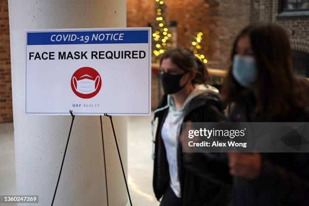 People pass a sign that reads "Face Mask Required" in a mall as COVID-19 cases surge in the city on December 21, 2021 in Washington, DC. District of...