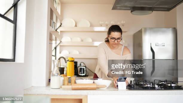 young woman cooking while looking at a recipe on the mobile phone at home - baking reading recipe stockfoto's en -beelden
