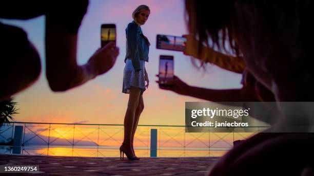 romantischer sonnenuntergang auf einer terrasse. schöne frau posiert im paillettenkleid für fotos von smartphones - paillettenkleid stock-fotos und bilder