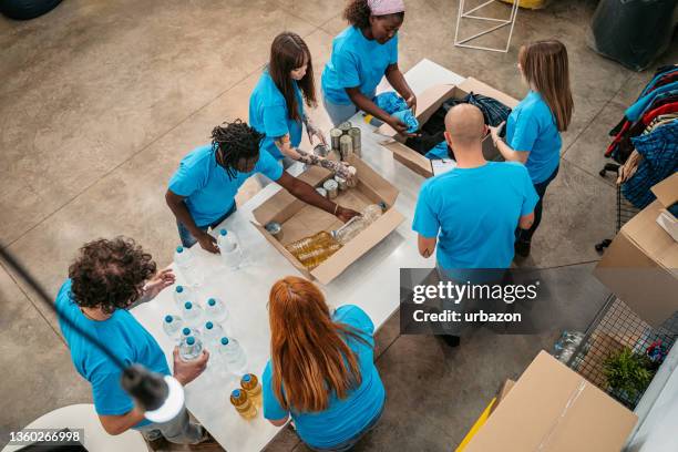 des bénévoles emballent de la nourriture et des vêtements dans des boîtes de dons - integration service photos et images de collection