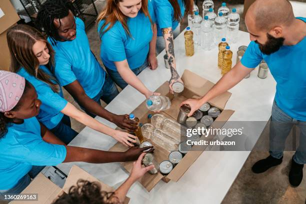 volunteers in donation center packing water and oil bottles and food in cans in boxes - philanthropist stock pictures, royalty-free photos & images