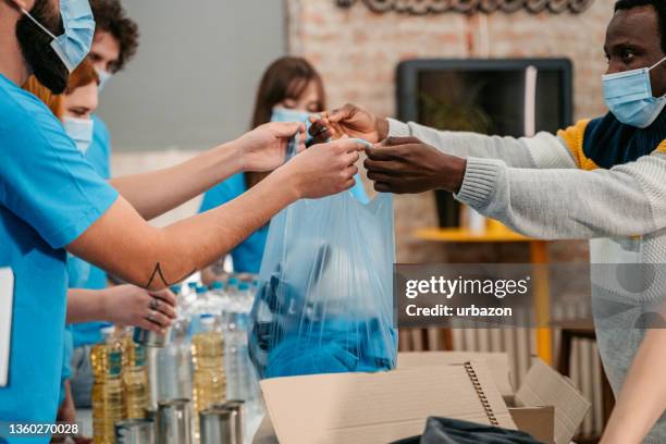 man receiving clothes from volunteer in charity center - philanthropist stock pictures, royalty-free photos & images