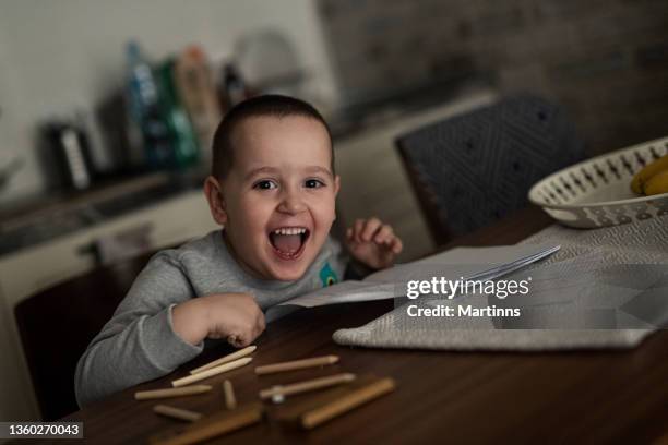 smiling young boy sitting at the kitchen table, drawing on pa paper and having fun - brown eye stock pictures, royalty-free photos & images