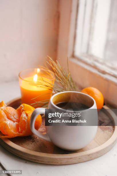 cozy winter home interior details, cup of coffee, wooden tray, tangerine and candle. window sill. still life for christmas. - coffee table reading mug stock pictures, royalty-free photos & images