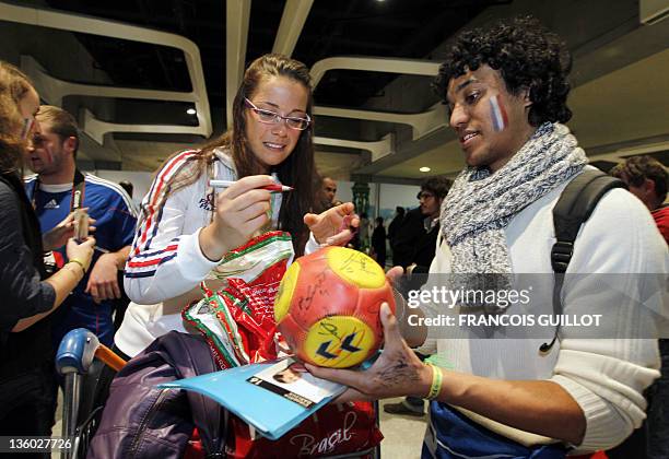 French goalkeeper Cléopâtre Darleux signs an autograph on a ball for a fan upon her arrival at the Roissy airport, near Paris on December 20, 2011...