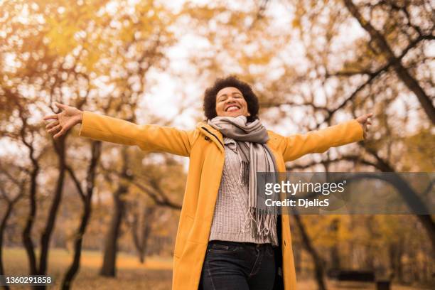 cheerful mid adult woman enjoying a beautiful autumn day in nature. - person of colour stock pictures, royalty-free photos & images