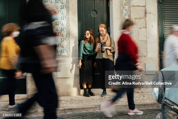2 female travelers standing on a doorstep of an azulejo-tiled house with a busy city street in front of them