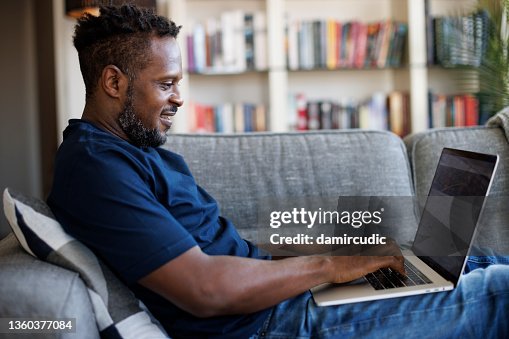 Uomo sorridente rilassato seduto sul divano e usando il laptop Uomo sorridente rilassato seduto sul divano e usando il laptop