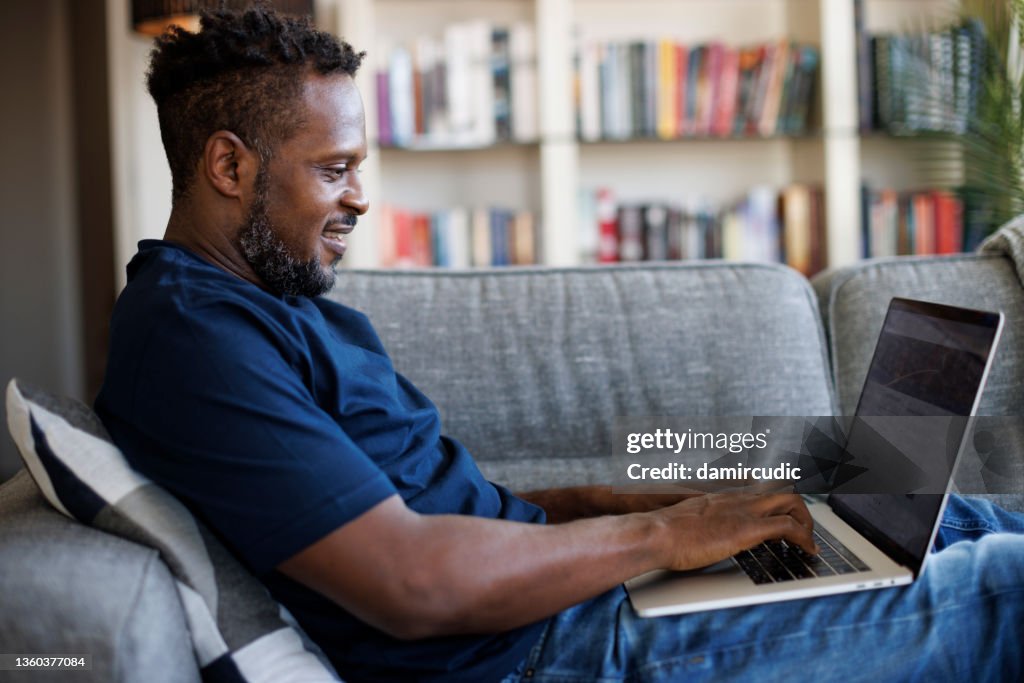 Relaxed smiling man sitting on sofa and using laptop
