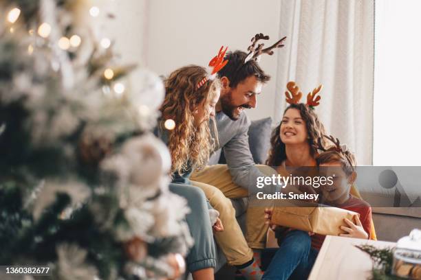 ein fröhlicher junge liegt auf dem schoß seiner mutter, auf dem boden. in seiner nähe, auf dem schlafsofa, liegen sein vater und seine schwester. er hat ein neujahrsgeschenk von seinen eltern erhalten und ist glücklich. - weihnachten geschenke stock-fotos und bilder