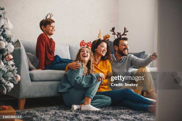 eine junge familie, die an weihnachten zeit miteinander verbringt. sie sind im wohnzimmer und schauen fern. - family tv stock-fotos und bilder