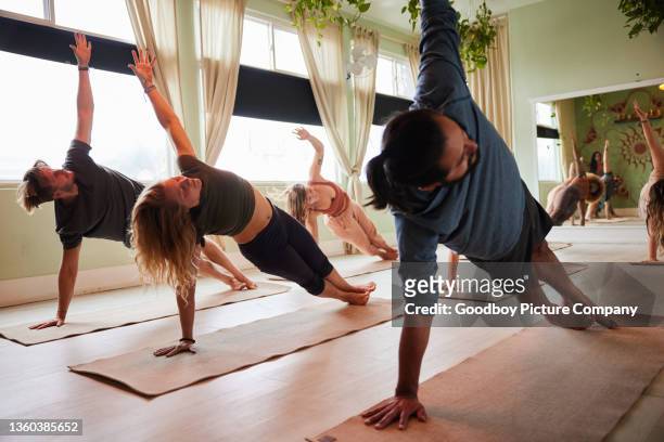 students doing the side plank pose on mats during a yoga class - side plank pose stock pictures, royalty-free photos & images
